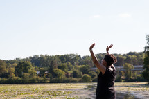 an African American woman with raised hands standing on a lake shore 