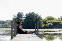 a woman with praying hands sitting at the end of a dock over a lake 