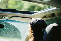 A person wearing a hat and riding in the passenger seat of a car.