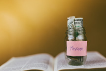 missions savings jar on the pages of a Bible 
