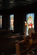 Communion wafer being broken over a chalice during a candle lit service.