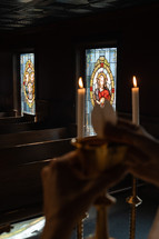 Out of focus shot of a communion wafer being broken with stained glass windows in the background.
