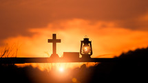 cross, Bible, and oil lamp silhouettes at sunset 