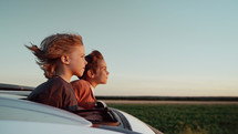 Adorable happy little kids stands in open car sunroof during road trip in countryside, rural landscape at summer. Concept of family leisure, active traveling. High quality