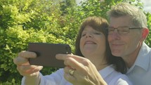 Active senior caucasian couple pulling funny faces taking selfies on a smartphone
