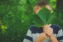 boy hiding behind a green leaf 