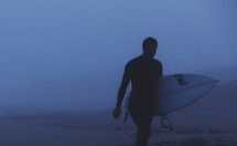 surfer walking on the beach holding a surf board