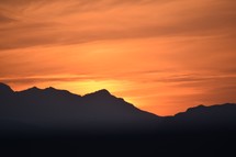 silhouettes of mountains at sunset against an orange sky 