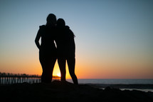 silhouettes of fiends hugging on a beach 