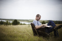 man sitting in a chair in a field reading