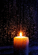 a burning candle behind a window covering in rain drops 