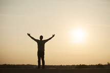 silhouette of a man standing with his arms raised in praise. 