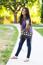 young woman with a purse standing on a sidewalk 