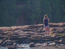 a woman standing on a rocky shore 