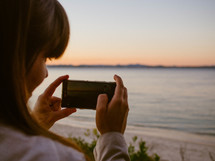 a woman taking pictures of a beach at sunset 