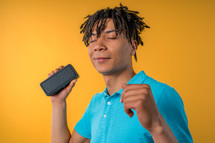 African american man dancing, enjoying on yellow studio background. Guy moves to rhythm of music. Young teenager listening to music by wireless portable speaker - modern sound system. High quality