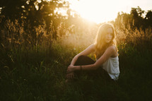 a young woman sitting in grass at sunset 
