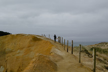 A person walking along the top of a large sand dune.