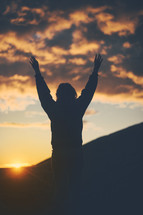 silhouette of woman with raised hands at sunset 