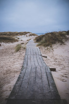 A board walk leading through sand dunes to the sea.