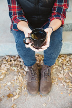 a woman sitting on a curb holding a mug of tea 