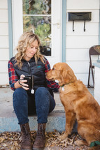 a woman sitting on a stoop in front of her house holding a mug of hot tea and her dog 
