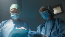 Doctor and nurse lay a surgical drape over the patient