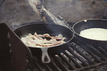 cooking bacon and eggs on skillets 