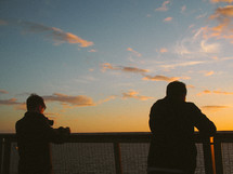 silhouettes of men looking over a railing at sunset 