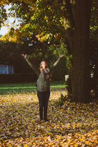 a woman standing in fall leaves with open arms 