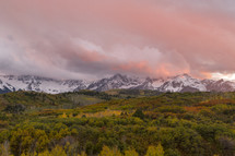 pink clouds over snow capped mountains and fall forest 