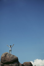 woman standing on top of a rock with her hands raised in worship to God