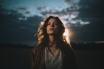 Portrait of a beautiful girl with long curly hair on the background of the setting sun