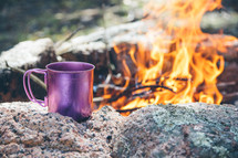 a coffee mug next to a camp fire 