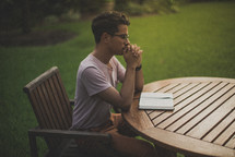 a young man reading a Bible in his backyard and praying 