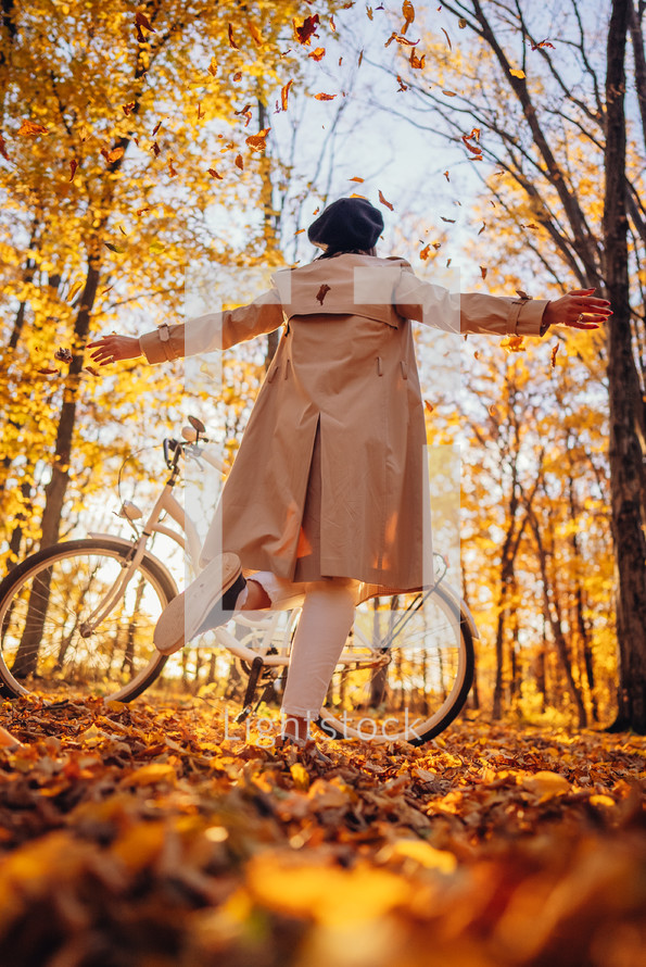 Young pretty woman enjoying autumn nature near vintage white bicycle. Lady having fun on orange nature fall background in park.