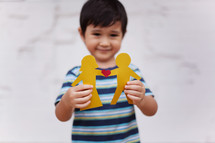 Concept of family with Asian Preschool-aged boy holding up a paper people chain of a traditional couple with a heart in between them.