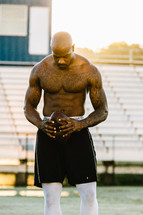 a shirtless man holding a football on a sports field 