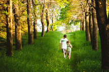 Two boys walking along a path of green grass lined by trees.