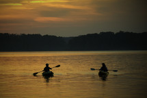 silhouettes of kayakers paddling at sunset 