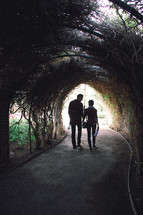 A man and woman walk together under a vine covered walkway,