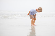 Boy standing in wet sand on the beach.