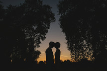 silhouette of a couple outdoors standing head to head at late sunset