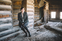 A woman sitting in an unfinished log house.