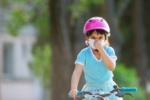 Little girl in protective medical mask rides a bicycle.