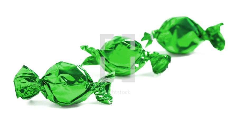 three green wrapped candies on a white background 