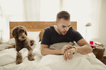 Man waking up late, in bed with dog.