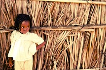toddler girl leaning against a hut 