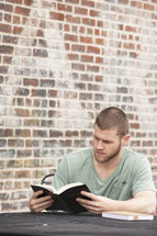 man reading a Bible sitting at an outdoor cafe