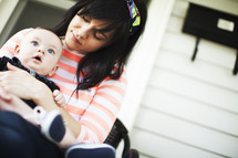 Baby sitting in mother's lap on a front porch.